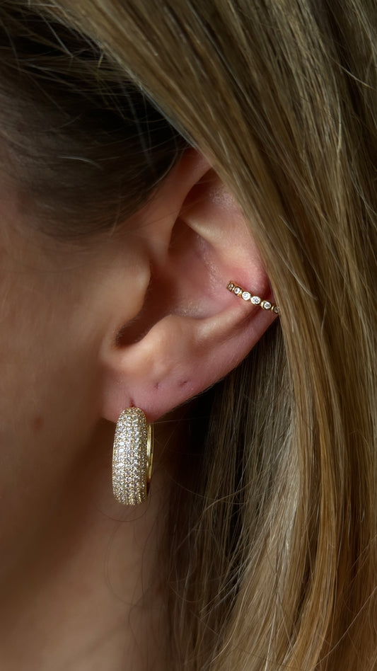 BOLD SPARKLE GOLDEN HOOPS are eye-catching earrings designed to make a statement. Crafted with a bold and substantial hoop design, these earrings are adorned with sparkling elements, likely gemstones, crystals, or intricate detailing that adds a touch of brilliance.
Material: Brass + 14K gold plated + zirconia
Measurements: .75 x .65 in