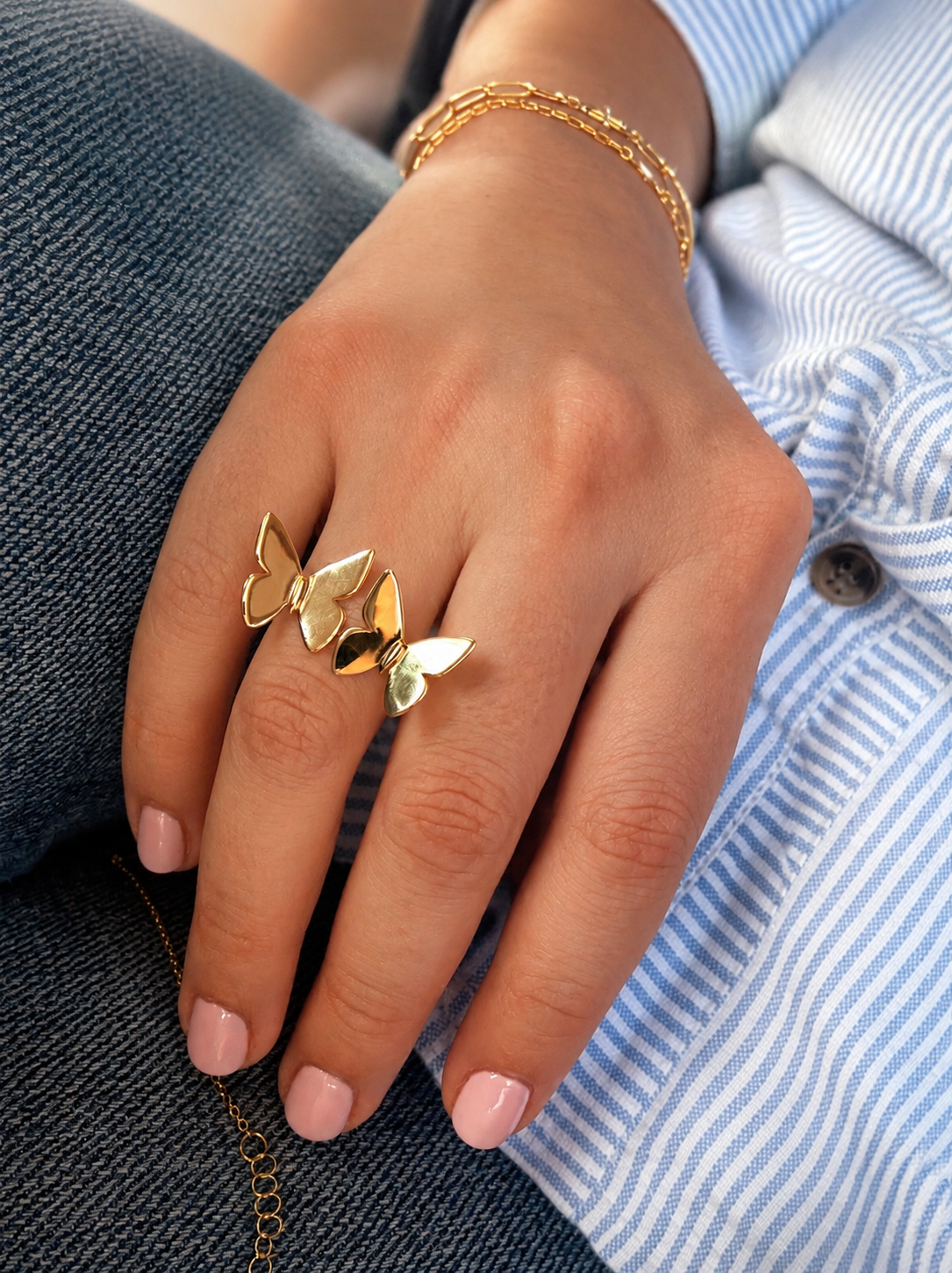 Gold ring with two butterflies design on a hand wearing denim jeans and a striped shirt.