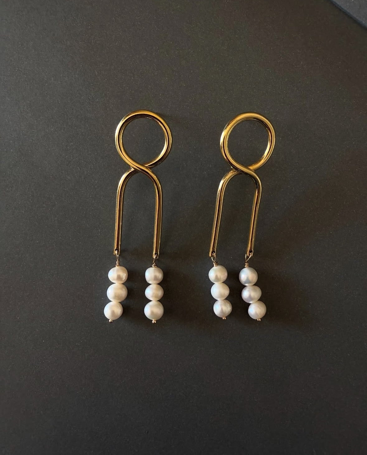 Gold Knot Pearl drop earrings with modern design on neutral background. 